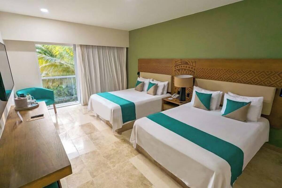 A hotel room with two beds, a desk, a chair, a TV, and a window with curtains.