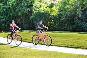 Two people riding bicycles on a paved path in a park with lush greenery in the background. - Viva Azteca by Wyndham, A Trademark All Inclusive Resort (PLAYA DEL CARMEN)