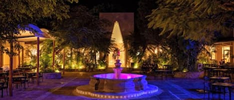 An outdoor area with a fountain, seating arrangements, and a well-lit environment.