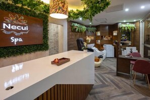 Un área de recepción con mostrador, una señalización en la pared y un espacio de espera con sillas y una mesa.