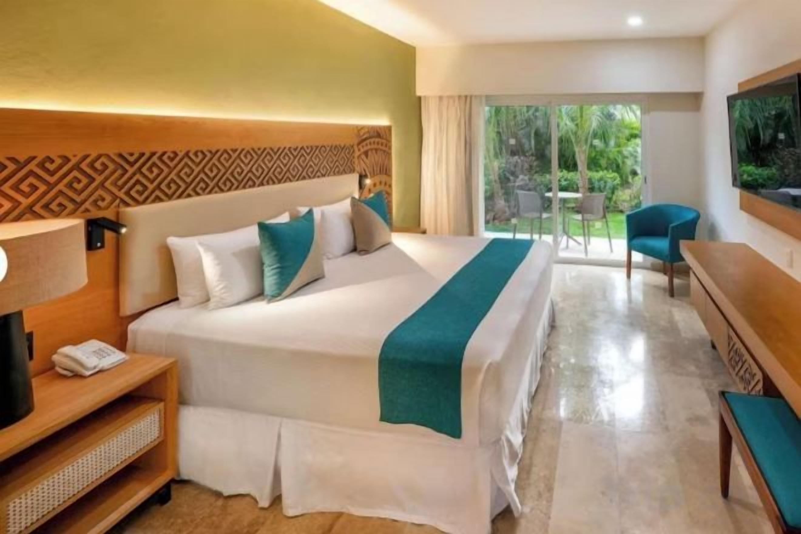 Habitación de hotel con una cama grande, una mesita de noche, una silla y vistas al exterior.