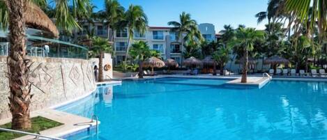 A swimming pool with clear blue water, surrounded by palm trees and lounge chairs.
