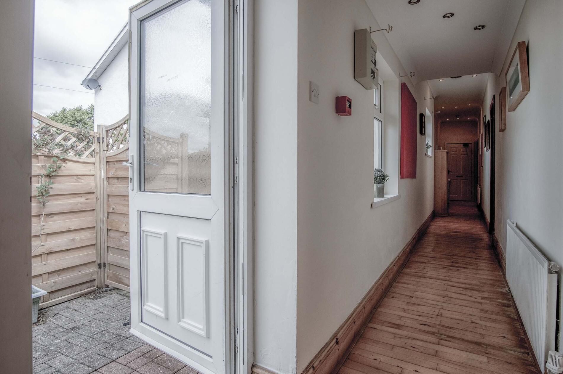 A narrow hallway with wooden flooring, a white door with glass panels, and a small window.