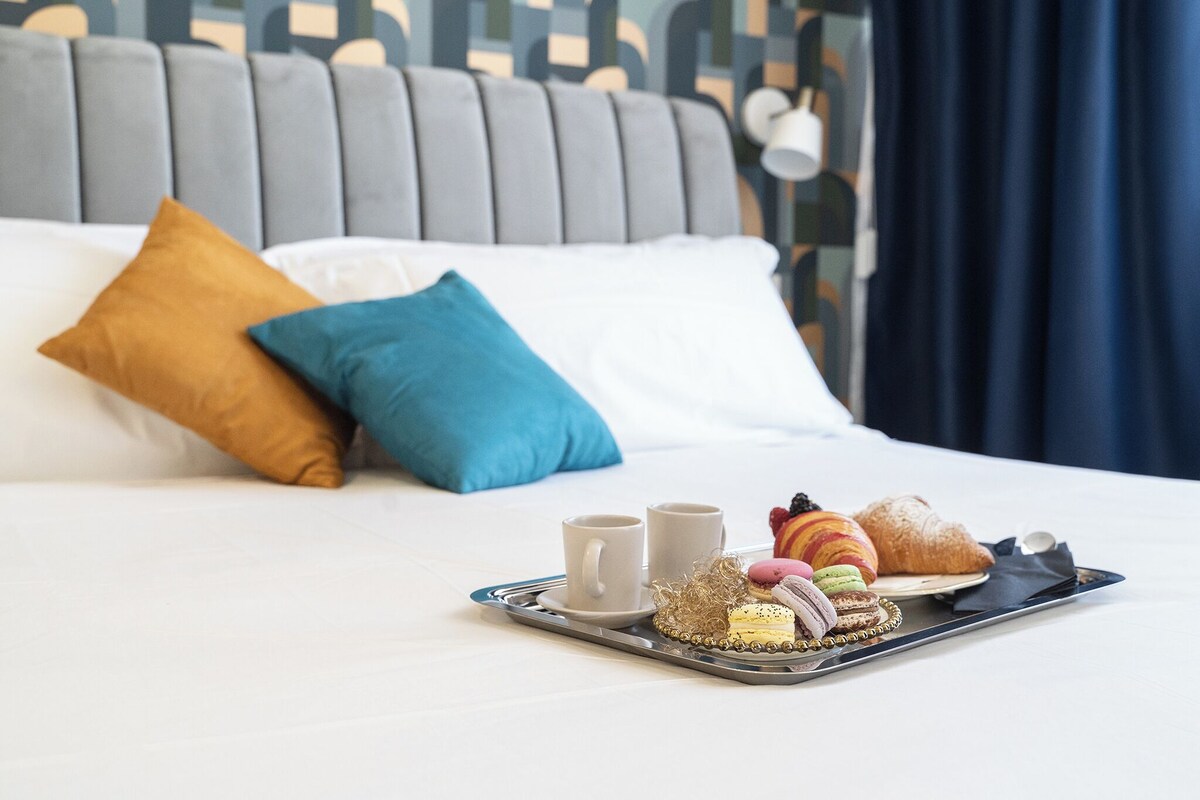 A neatly made bed with a tray of pastries, two cups, and a croissant on a hotel room.