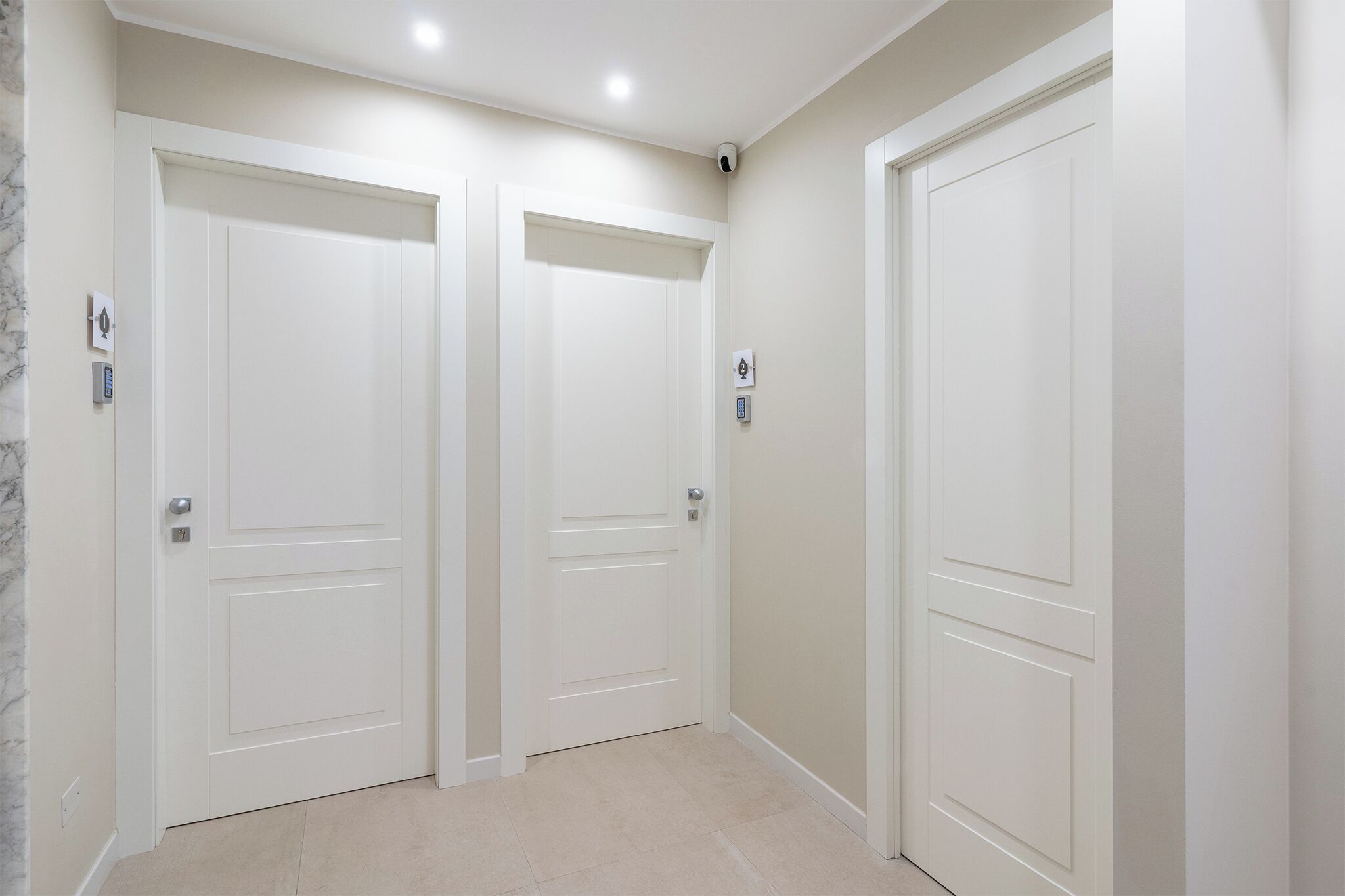 A hallway with three white doors, each with a doorbell and a light switch.