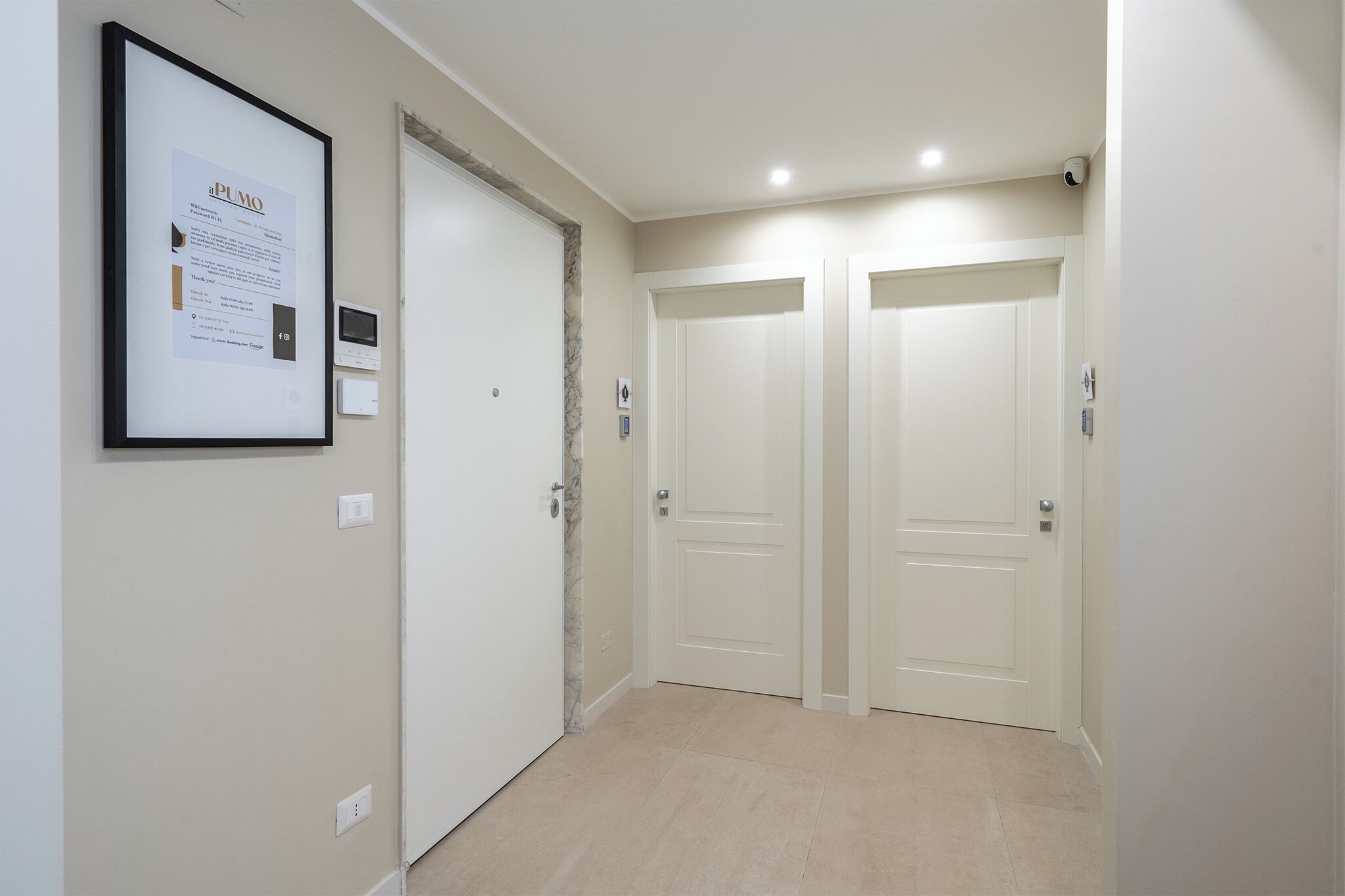 Un couloir avec deux portes blanches, un avis encadré accroché au mur et un interrupteur.