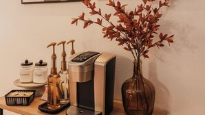 Un comptoir de cuisine avec une machine à café, un vase contenant des feuilles rouges et deux tableaux abstraits accrochés au mur.