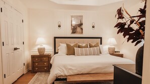 Une chambre à coucher avec un lit, des tables de chevet, des lampes, un tapis et une plante.