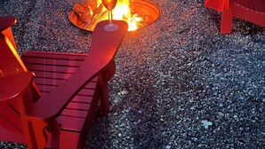 Un pozo de fuego rodeado por cuatro sillas Adirondack rojas, sobre grava.