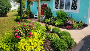 Una casa con un jardín cuidado, un porche con sillas y una puerta roja.