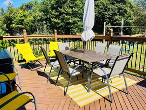 Une terrasse extérieure avec une table et des chaises, entourée d’une clôture en bois et de verdure.