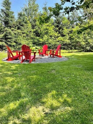 Relax in a serene outdoor space surrounded by lush greenery and comfortable Adirondack chairs.