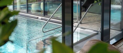 Una piscina interna, vetrata, con ringhiere in metallo e vista sulla zona circostante.