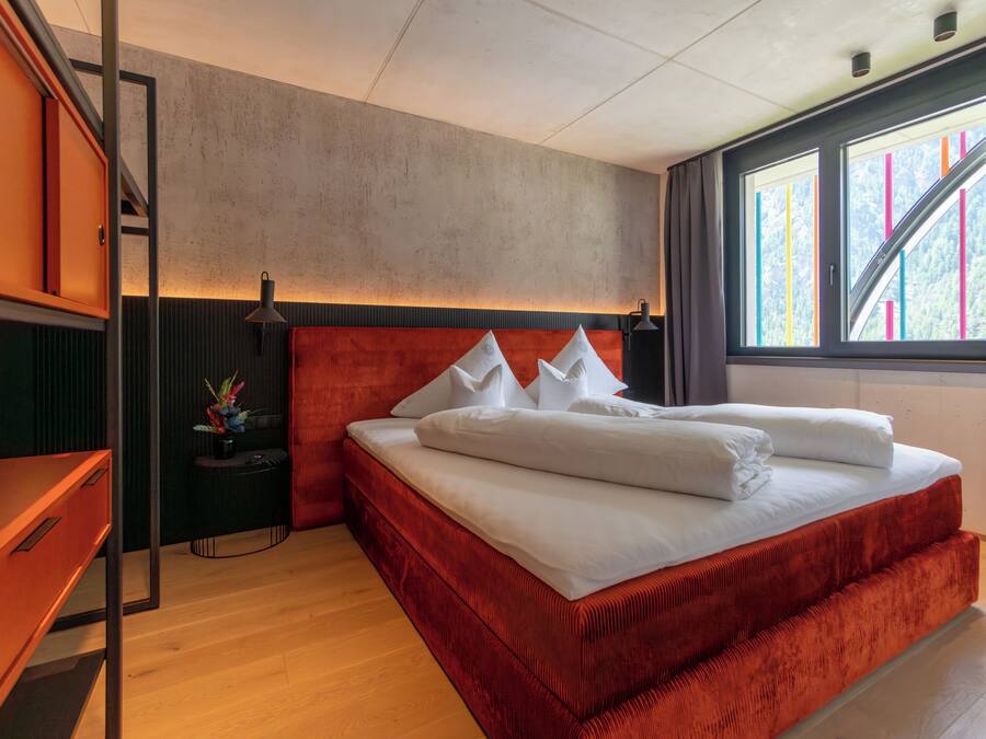 Un dormitorio moderno con una cama grande, un escritorio y una ventana con vista a edificios coloridos.