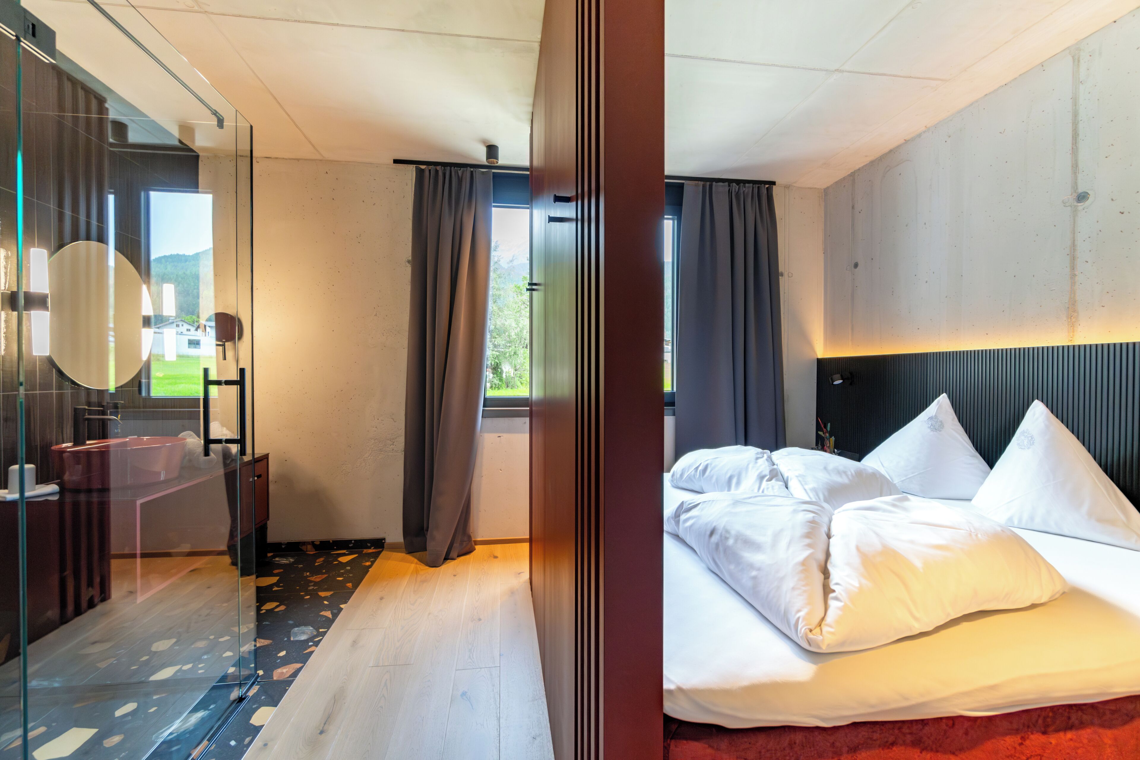 Habitación de hotel moderna con una cama grande, cabina de ducha de vidrio y vistas al exterior.