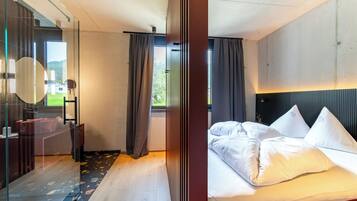 Habitación de hotel moderna con una cama grande, cabina de ducha de vidrio y vistas al exterior.