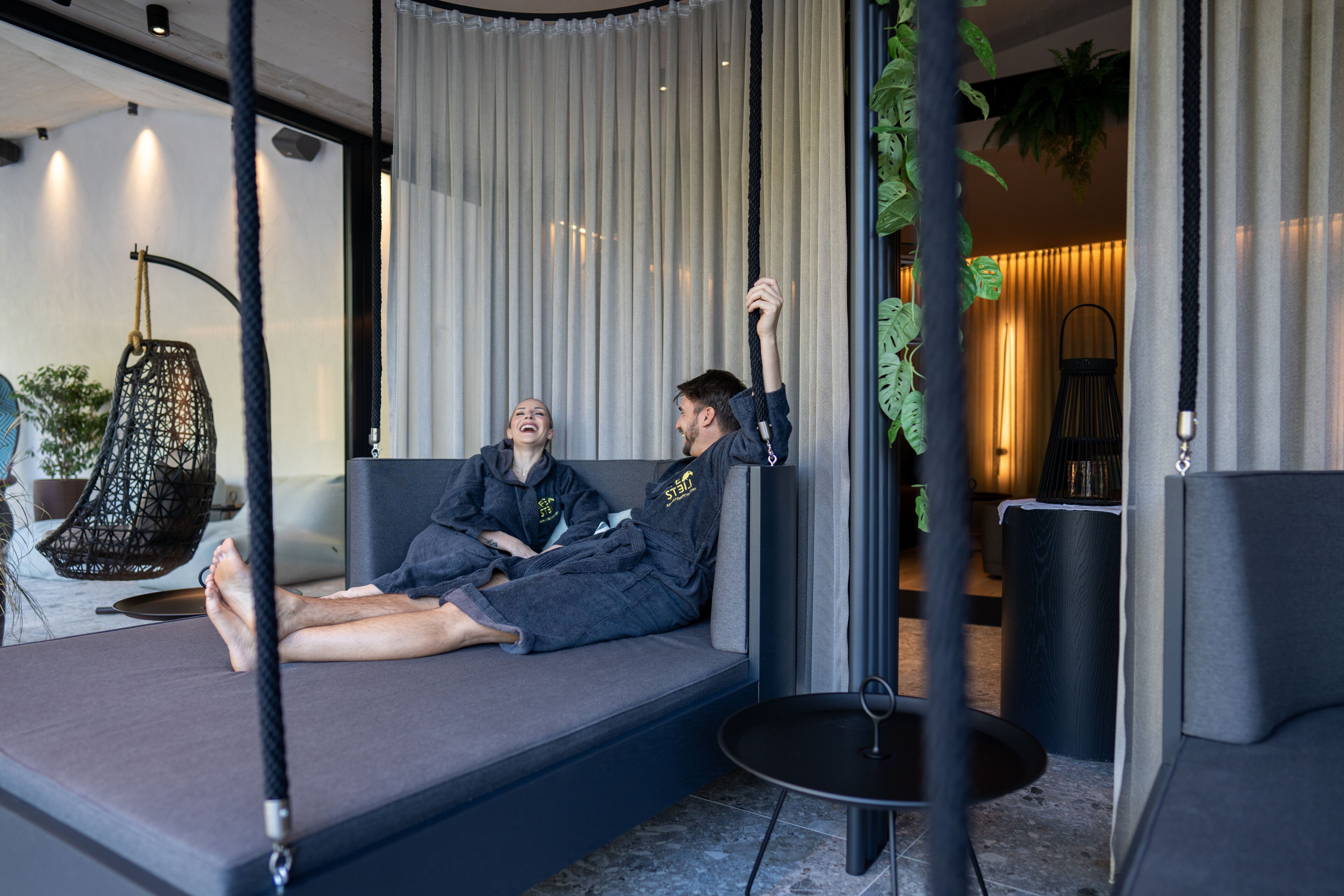 Un salon moderne avec un canapé, un fauteuil suspendu et une petite table.