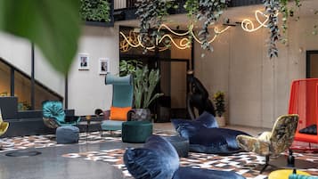 A modern lounge area with a geometric patterned floor, various seating options including a teal armchair, a black chair, and a red couch.