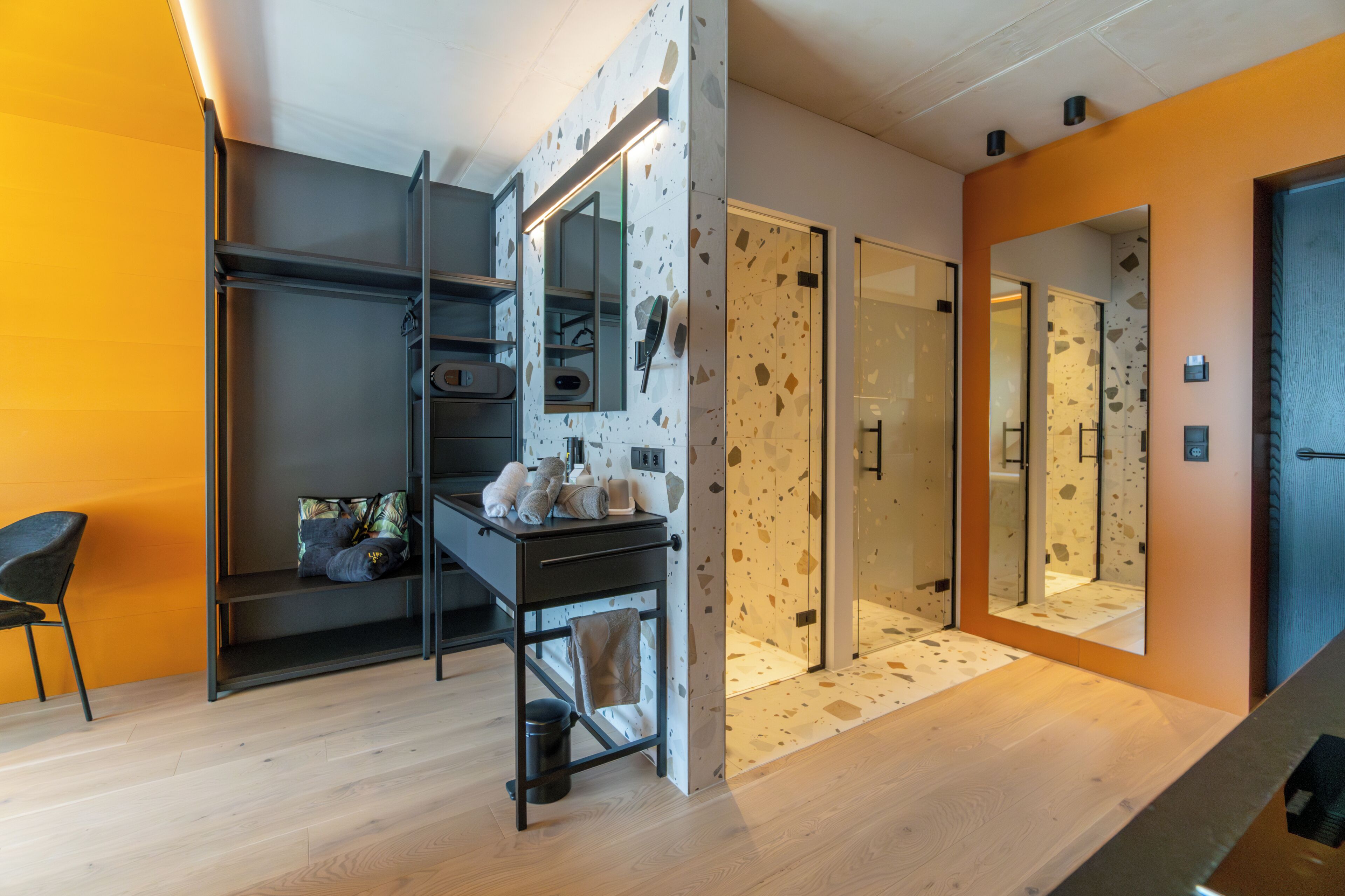 Un baño moderno con ducha de vidrio, lavamanos con artículos de aseo y un perchero para toallas.