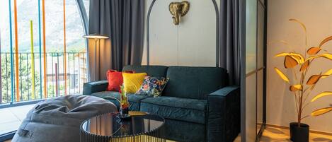 Ein modernes Wohnzimmer mit einem dunkelgrünen Sofa, bunten Kissen, einem schwarzen Couchtisch, einem grauen Sitzsack und einem dekorativen Elefantenkopf an der Wand.