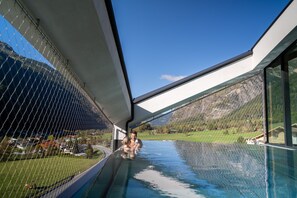 Una piscina infinita con borde de cristal, vistas a la montaña, cielo despejado y diseño arquitectónico moderno.