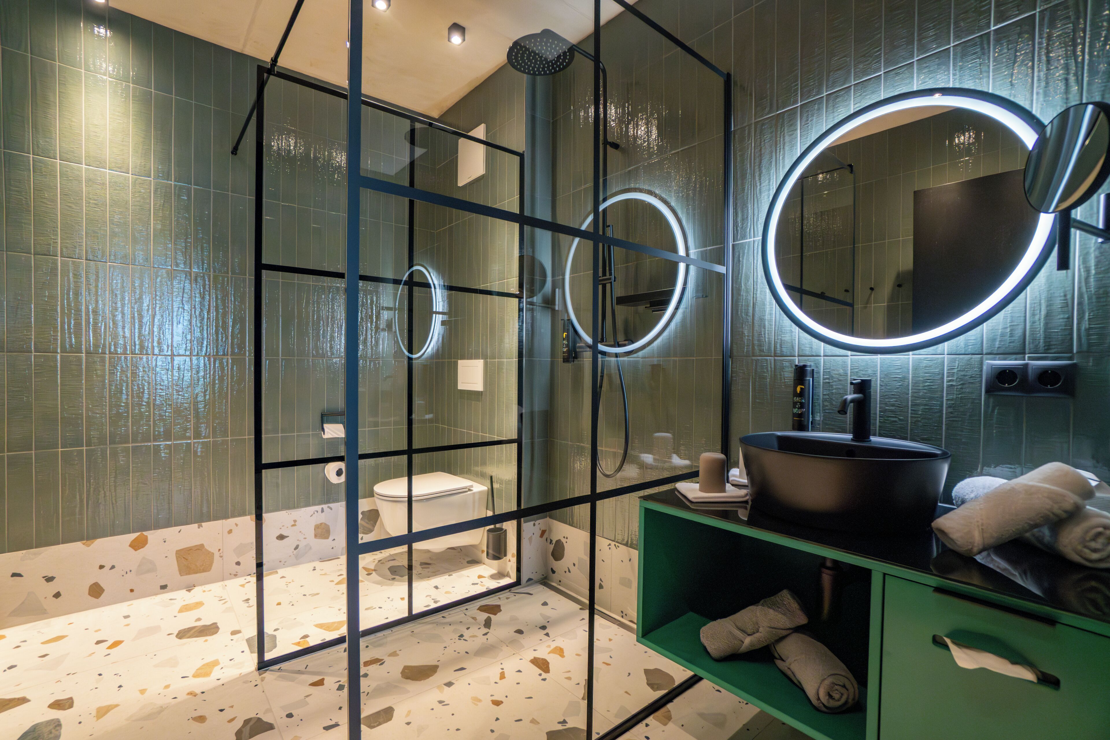 Un bagno moderno con doccia a vetro, specchio rotondo, lavandino e mobile bagno verde.