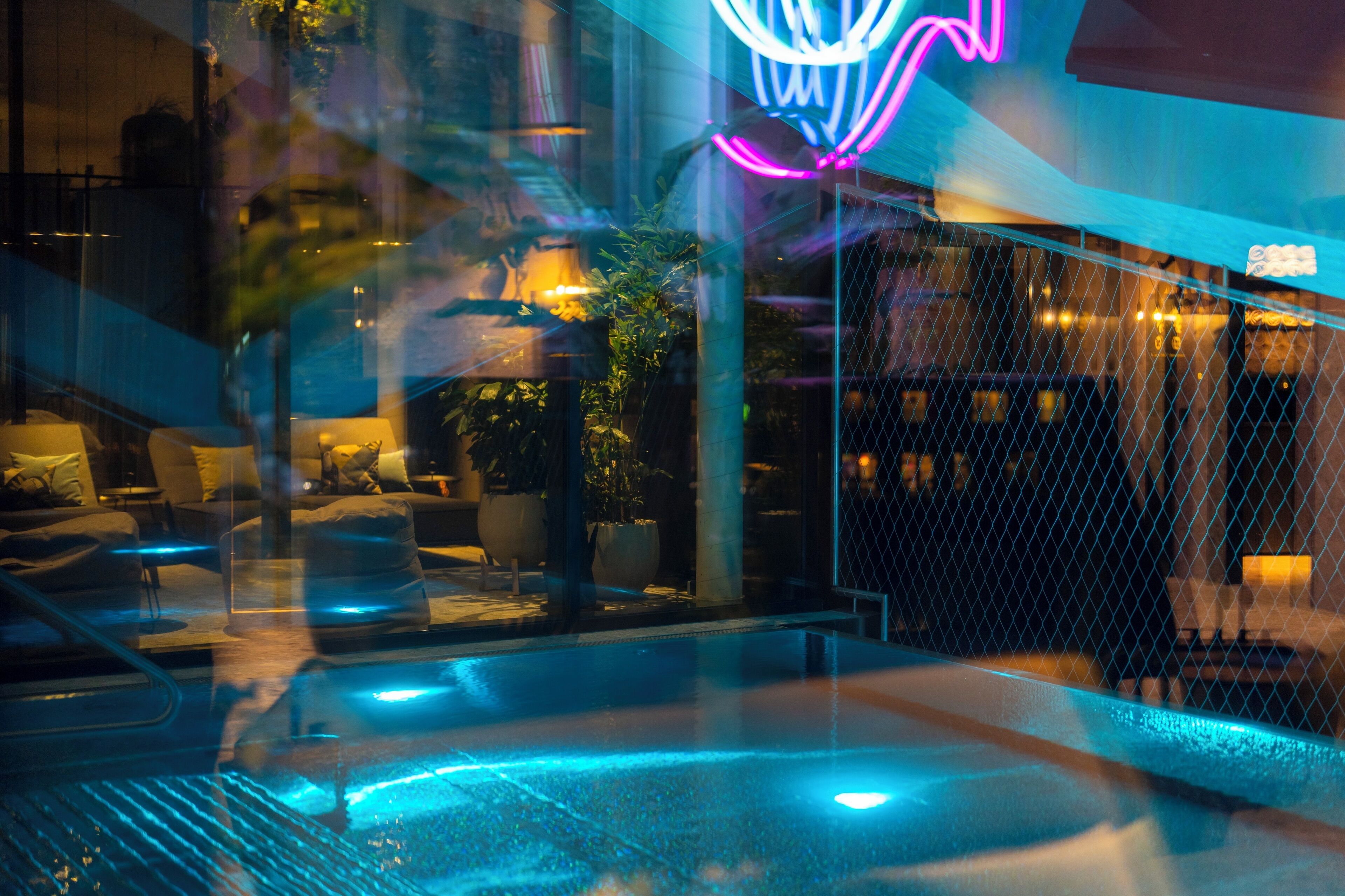 Un espace piscine intérieure moderne, doté d’une paroi vitrée, de sièges et d’un panneau lumineux au néon.