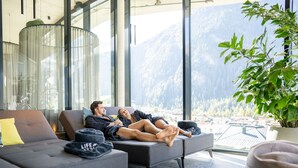 A modern living room with a sofa and a large window offering a mountain view. - LIFESTEIL Appartementresort (Umhausen)