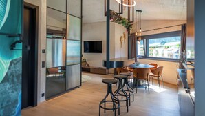 A modern interior with a dining area, a TV mounted on the wall, and a large window providing a view of the outside. - LIFESTEIL Appartementresort (Umhausen)