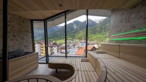 A wooden spa area with a view of a mountain village. - LIFESTEIL Appartementresort (Umhausen)