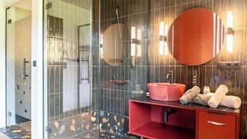 Een moderne badkamer met een douchecabine van glas, een rode wastafel met een roze wasbak en een grote spiegel.