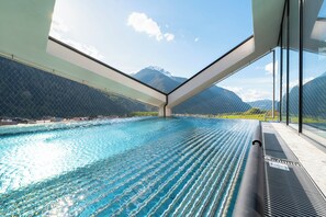 An indoor swimming pool with a mountain view, a glass ceiling, and a metal railing. - LIFESTEIL Appartementresort (Umhausen)