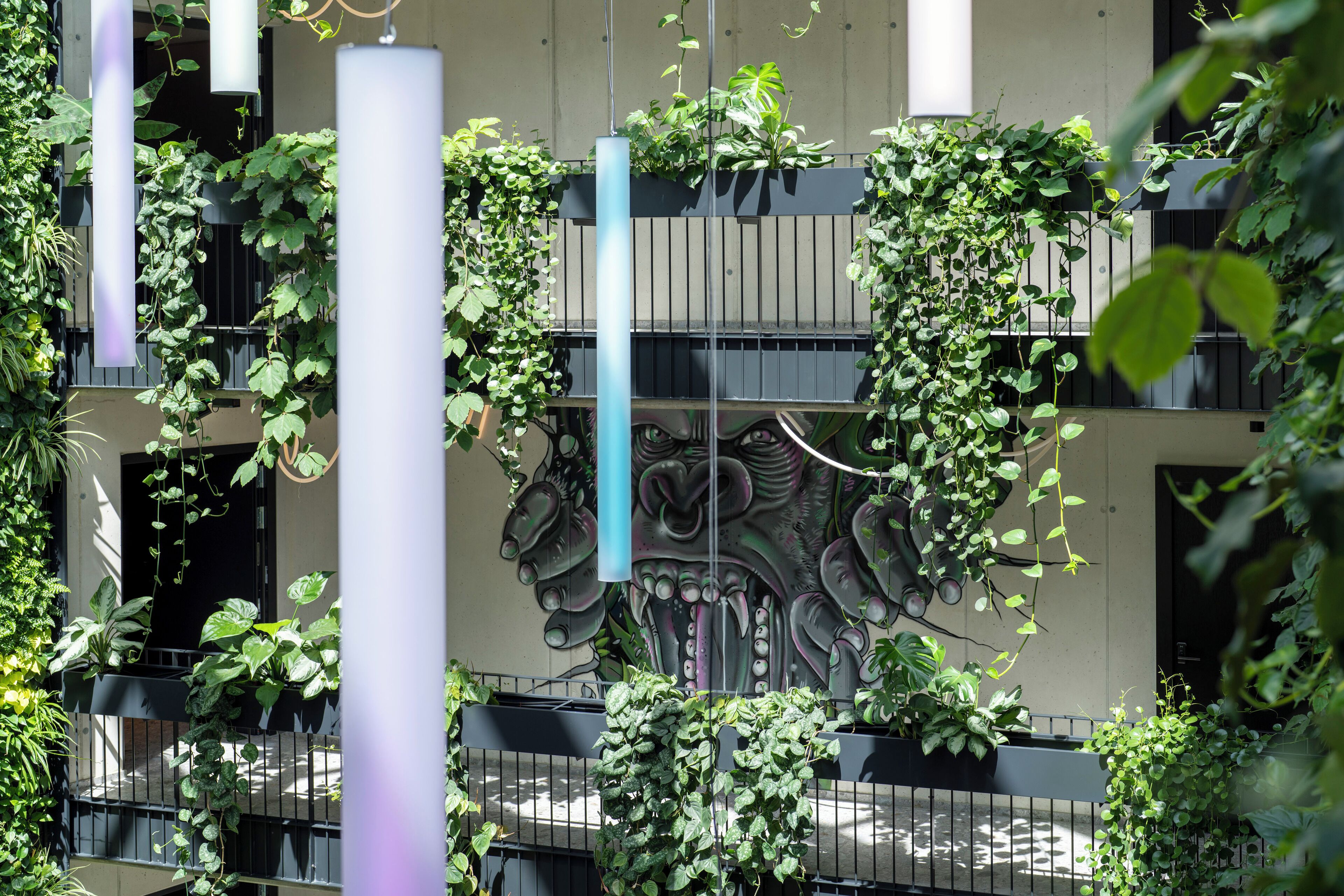 A building with balconies covered in greenery, a mural with a dragon design, and hanging plants.