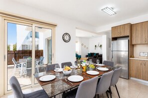 A modern kitchen with a built-in refrigerator, a dining area with a glass table, and a sliding glass door leading to an outdoor patio.