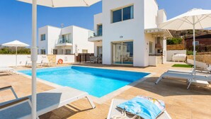 Un edificio moderno de dos pisos con piscina, mobiliario exterior y vistas del paisaje circundante.