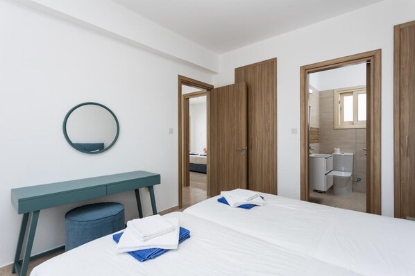 Habitación de hotel con cama, escritorio, espejo y baño visible a través de una puerta abierta.