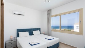 Un dormitorio con dos camas, una mesita de noche, un equipo de aire acondicionado y una ventana con vistas al mar.
