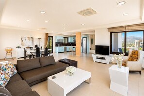 Ein modernes Wohnzimmer mit Sofa, Couchtisch und Fernseher, verbunden mit einer Küche und einem Essbereich.