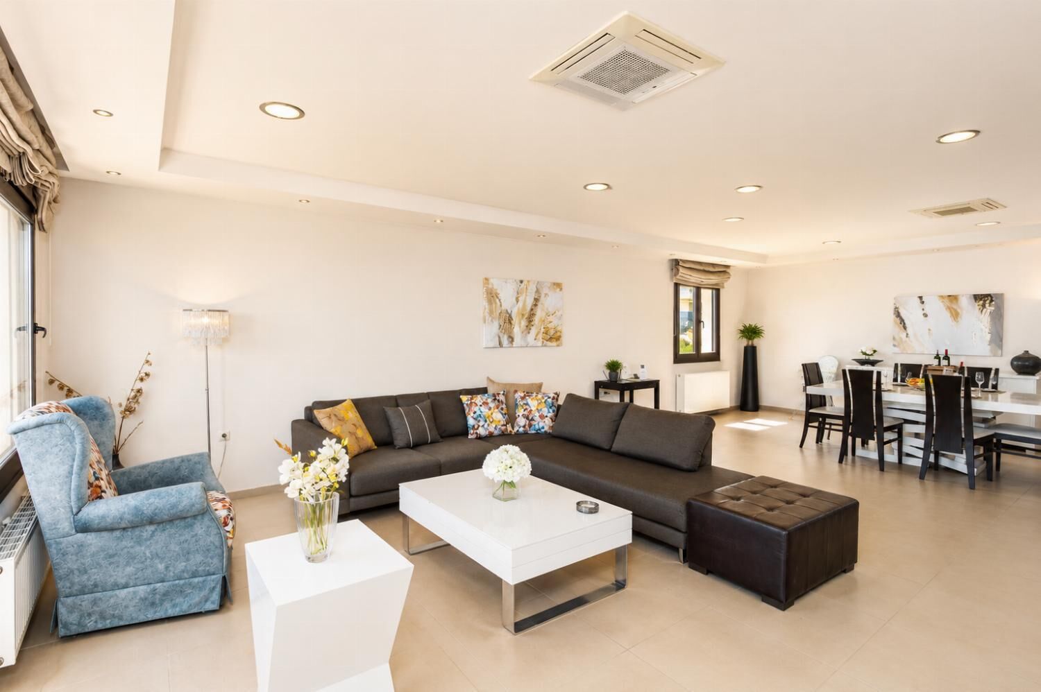 Ein modernes Wohnzimmer mit einer Couch, einem Couchtisch und einem Sessel, ein Essbereich mit Tisch und Stühlen sowie ein großes Fenster, das für natürliches Licht sorgt.