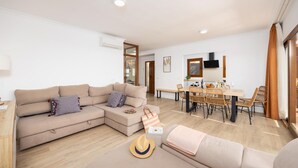Ein modernes Wohnzimmer mit einer Eckcouch, einem Esstisch mit Stühlen und einer durch eine offene Tür einsehbaren Küche.