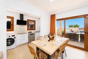 Una cucina moderna con lavatrice integrata, una zona pranzo con tavolo imbandito per quattro persone e una porta scorrevole in vetro che dà su un patio esterno.