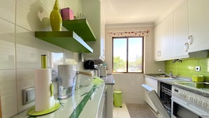 Une cuisine avec des armoires blanches, un plan de travail vert, une fenêtre donnant sur un beau paysage et un four encastré.