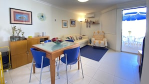 Un salon comprenant une table à manger, des chaises bleues, un canapé, un fauteuil à motifs et une vue sur l’extérieur grâce à une porte vitrée.