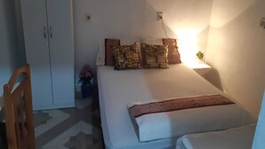 Een slaapkamer met een bed, kussens, een nachtkastje, een lamp, een garderobe en een kleine plant.
