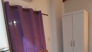 Een kamer met een paars douchegordijn, een houten stoel, een witte inloopkast en een betegelde vloer.