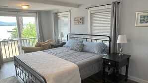 A bedroom with a bed, bedside table, lamp, and a view of the outdoors. - Lakefront home on Ossipee Lake with dock and gorgeous views  (Ossipee)