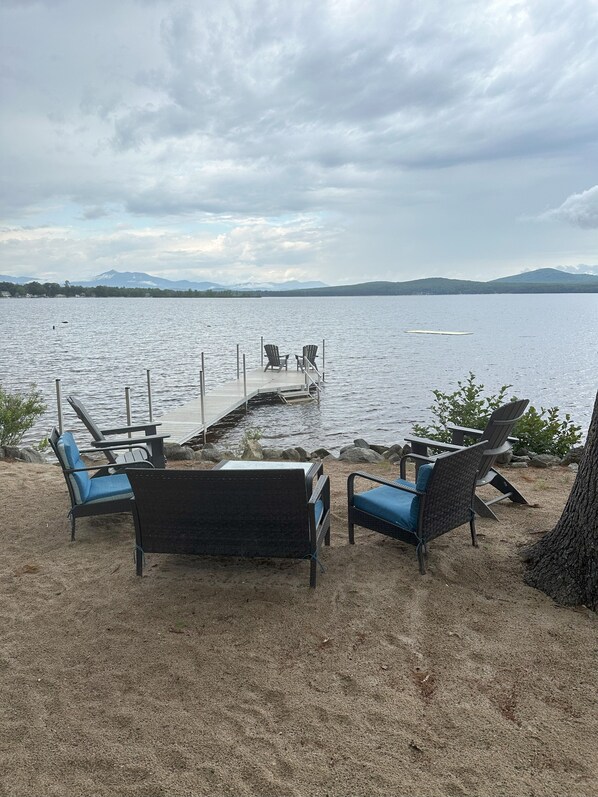A lakeside seating area with chairs and a dock extending into the water. - Lakefront home on Ossipee Lake with dock and gorgeous views (Ossipee)