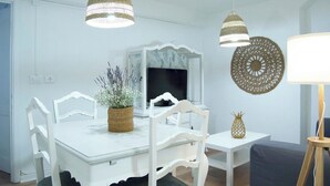 A dining area with a white table, white chairs, a woven basket with flowers, a pineapple, and decorative wall art. - ABASTOS "Ferrol" Apartment (Ferrol)