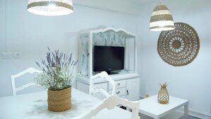 A modern living room with a white sofa, a coffee table, and a TV on a white cabinet. There are two hanging lamps and a decorative wall piece. - ABASTOS "Ferrol" Apartment (Ferrol)