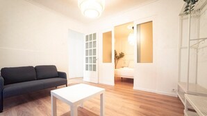 A modern living room with a dark sofa, a white coffee table, and a wooden floor. There is a door leading to another room with a bed and a lamp. - Apartment Sol "Ferrol". (Ferrol)